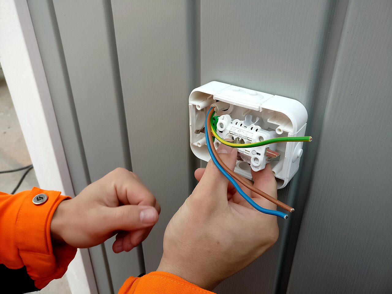 Electrician wiring an outdoor power socket with brown, blue and green-yellow earth cable